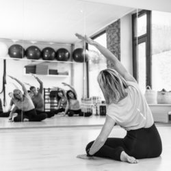 dedos_miroir_72dpi Posture de pilates: josiane buchart face au miroir de la salle du studio pilates et yoga satigny en position du stretching sur le coté avec un groupe d'élèves hommes et femmes